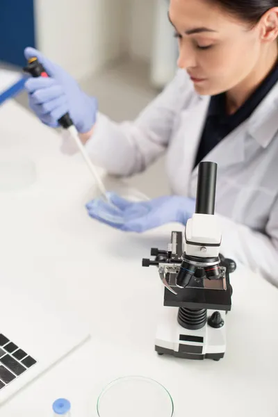 Microscopio cerca de laptop y científico borroso trabajando en laboratorio - foto de stock