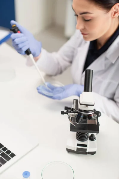 Microscopio cerca de laptop y científico borroso trabajando en laboratorio - foto de stock