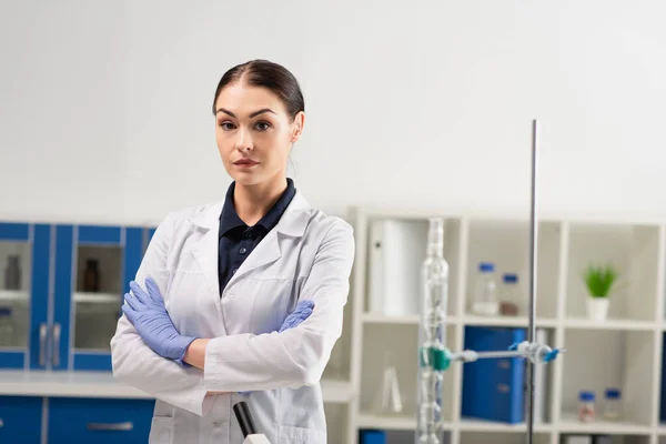 Cientista em luvas de látex olhando para a câmera perto de equipamentos em laboratório — Fotografia de Stock