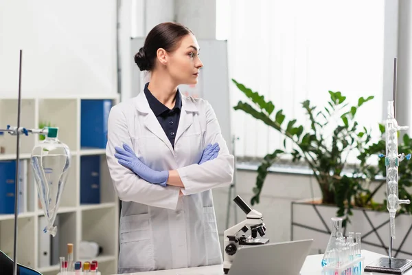 Vista lateral del científico de capa blanca de pie cerca del equipo en la mesa de trabajo en el laboratorio - foto de stock