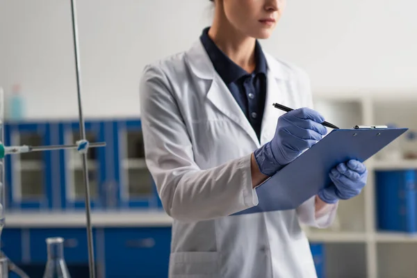 Cropped view of scientist writing on clipboard in laboratory — Stock Photo