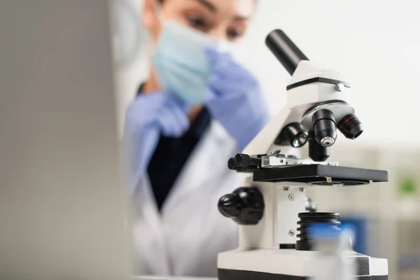 Microscópio perto de cientista borrado em máscara médica em laboratório — Fotografia de Stock