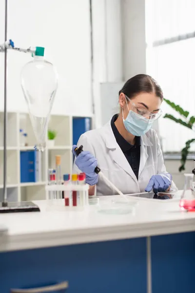 Cientista usando tablet digital e segurando pipeta eletrônica perto de equipamentos médicos em laboratório — Fotografia de Stock