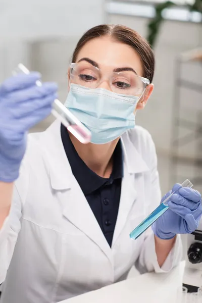 Cientista em óculos, máscara médica e luvas de látex segurando tubos de ensaio em laboratório — Fotografia de Stock