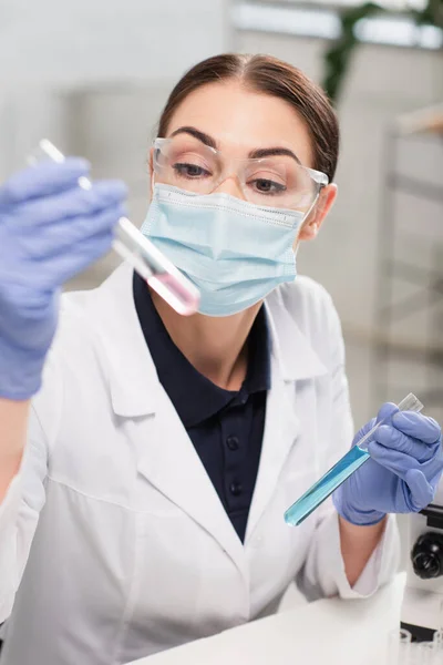 Scientist in goggles, medical mask and latex gloves holding test tubes in lab — Stock Photo