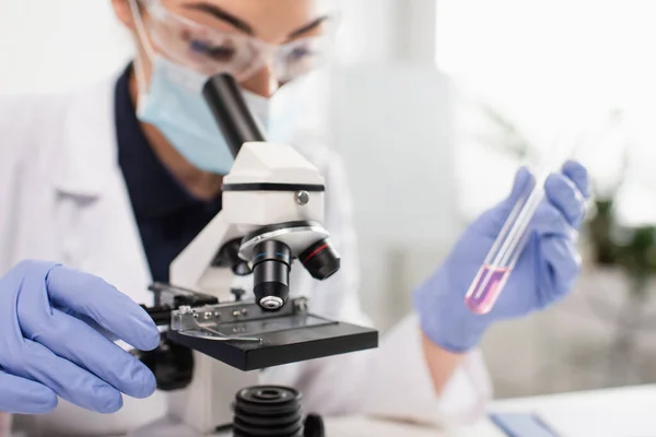 Microscópio perto de cientista em luvas de látex segurando tubo de ensaio em laboratório — Fotografia de Stock