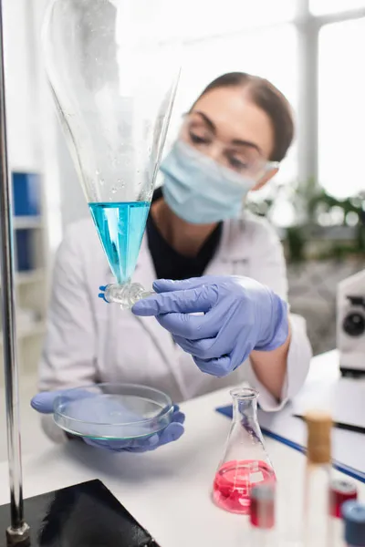 Científico en guantes de látex trabajando con matraz y placa petri en laboratorio - foto de stock