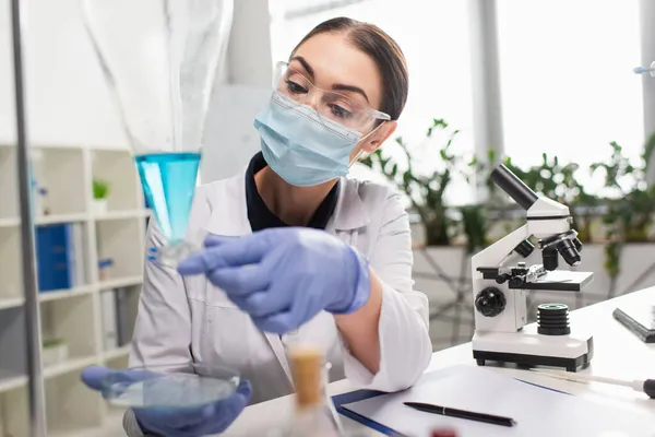 Scientist in goggles working with petri dish and flask near microscope in lab — Stock Photo