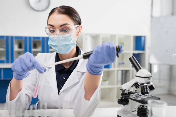 Científico en gafas de seguridad trabajando con tubo de ensayo y pipeta electrónica en laboratorio - foto de stock