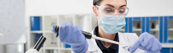 Científico en máscara médica y guantes de látex trabajando con pipeta en laboratorio, pancarta - foto de stock