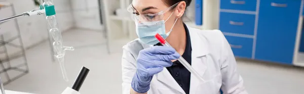 Wissenschaftler mit medizinischer Maske hält PCR-Test in der Nähe von Mikroskop im Labor, Banner — Stockfoto