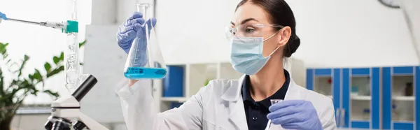 Científico en guantes de látex sosteniendo frascos cerca del microscopio en el laboratorio, pancarta - foto de stock