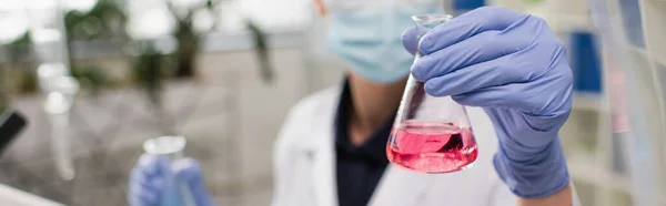 Vista recortada de cientista desfocado em luvas de látex segurando frasco em laboratório, banner — Fotografia de Stock