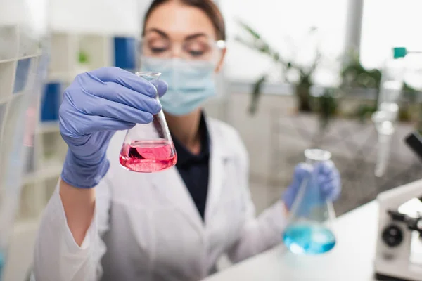 Científico borroso en guantes de látex sosteniendo matraz en laboratorio - foto de stock