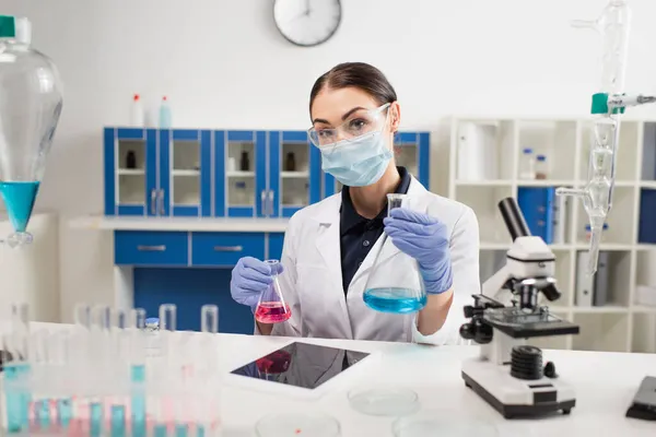 Científico sosteniendo frascos cerca de la tableta digital con pantalla en blanco y microscopio en el laboratorio — Stock Photo