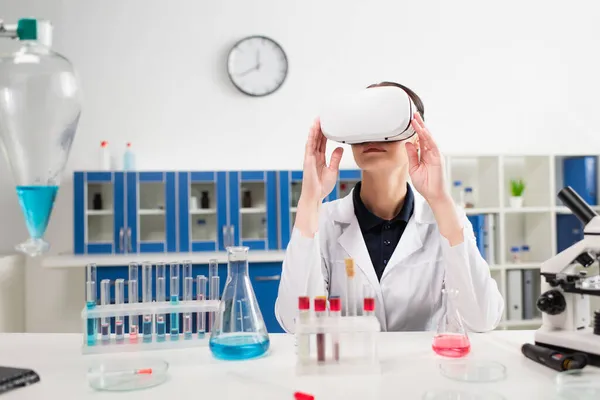 Scientifique dans le casque vr près du microscope et des éprouvettes avec des échantillons de sang en laboratoire — Photo de stock