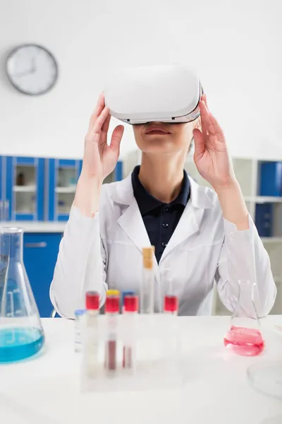 Smiling scientist in virtual reality headset near blurred test tubes and flasks in lab — Stock Photo