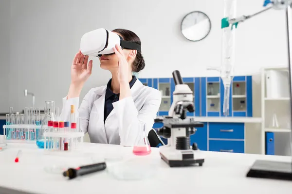 Scientist in white coat and vr headset near microscope and test tubes in laboratory — Stock Photo