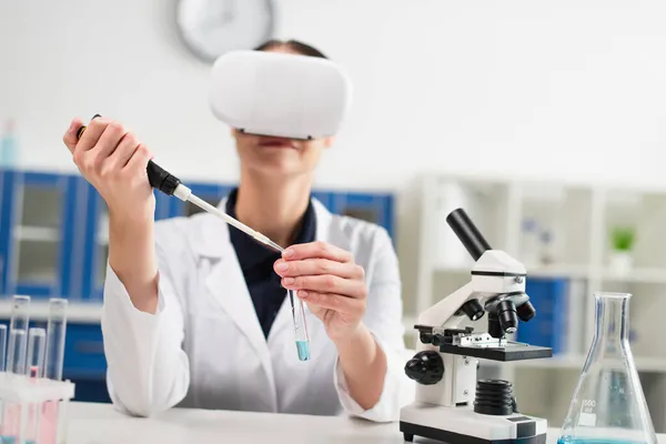 Reagenzglas und elektronische Pipette in den Händen verschwommener Wissenschaftler im vr-Headset bei der Arbeit im Labor — Stockfoto