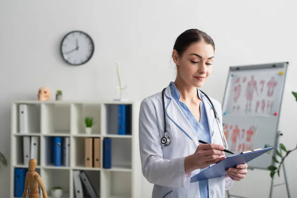 Morena médico escribiendo en portapapeles en la clínica - foto de stock