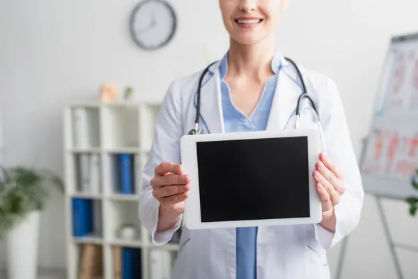 Vista recortada del médico sonriente sosteniendo tableta digital con pantalla en blanco en la clínica - foto de stock