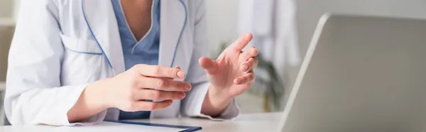 Vista ritagliata del medico che fa videochiamate su laptop sfocato vicino agli appunti in clinica, banner — Foto stock