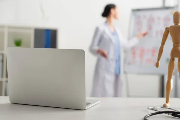 Laptop near stethoscope near blurred doctor in clinic — Stock Photo