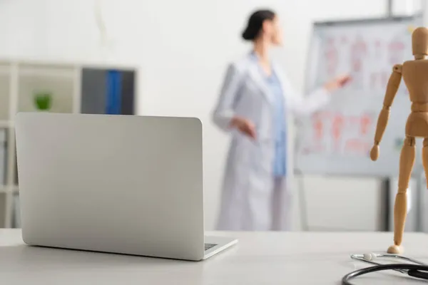 Laptop perto de estetoscópio perto de médico borrado na clínica — Fotografia de Stock