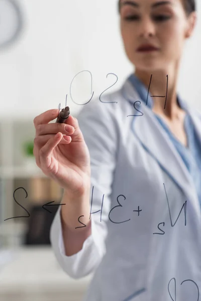 Blurred scientist writing chemical formulas with felt pen on glass board — Stock Photo