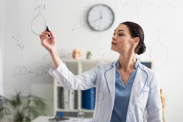Брюнетка вчений пише на скляній дошці в клініці — стокове фото