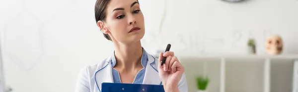 Morena, médico pensativo sosteniendo fieltro pluma y portapapeles en el hospital, pancarta - foto de stock