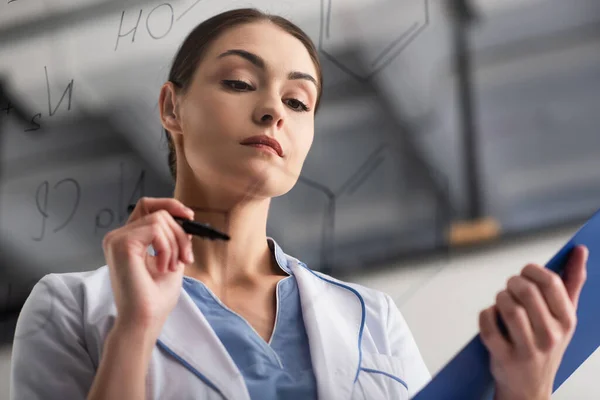 Vue à angle bas du scientifique avec stylo feutre près de formules floues sur panneau de verre — Photo de stock