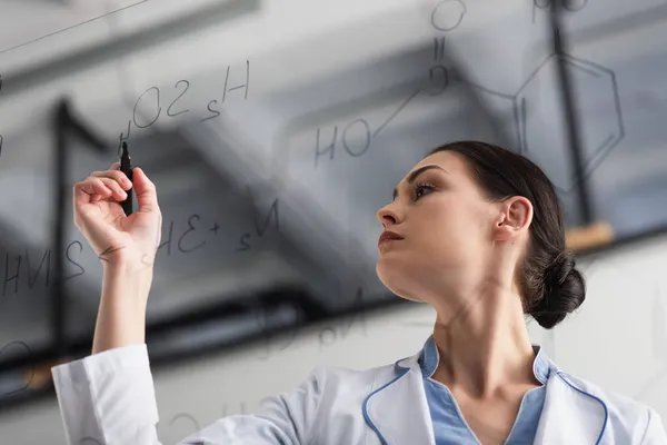 Low angle view of chemist writing formulas on glass board — Stock Photo