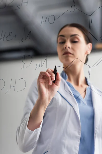 Low angle view of blurred scientist wiring chemical formulas on glass board — Stock Photo