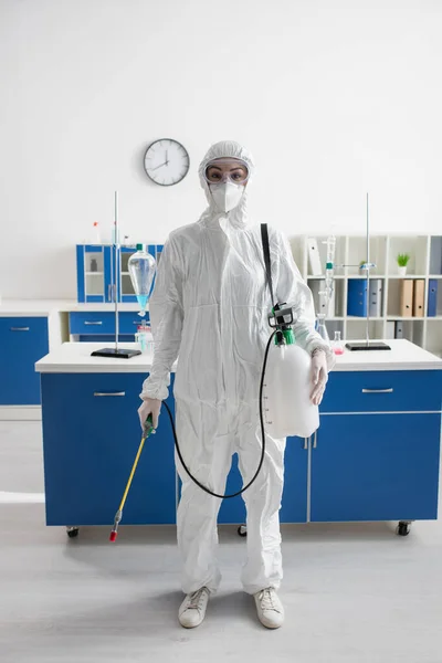 Wissenschaftler im Warnanzug blickt in Kamera, während er Sprayer im Labor hält — Stockfoto