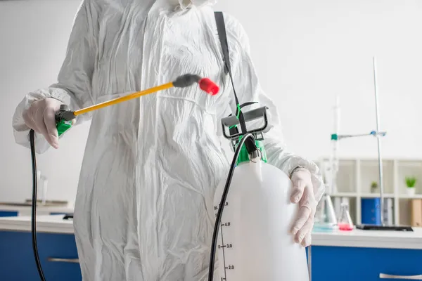 Visão cortada do cientista em terno protetor segurando pulverizador ao fazer a desinfecção do laboratório — Fotografia de Stock