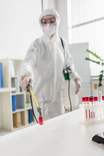 Blurred doctor in protective suit making disinfection of laboratory with sprayer — Stock Photo