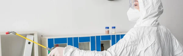 Лікар в окулярах і матовий костюм робить дезінфекцію лабораторії розпилювачем, банер — Stock Photo