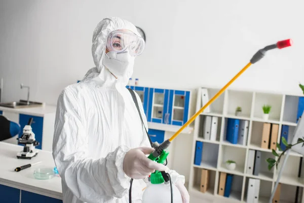 Arzt in Schutzbrille und Schutzanzug hält Sprayer während Desinfektion im Labor — Stockfoto