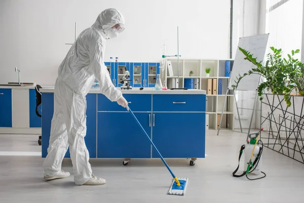 Side view of doctor in hazmat suit cleaning floor in laboratory with mop — Stock Photo