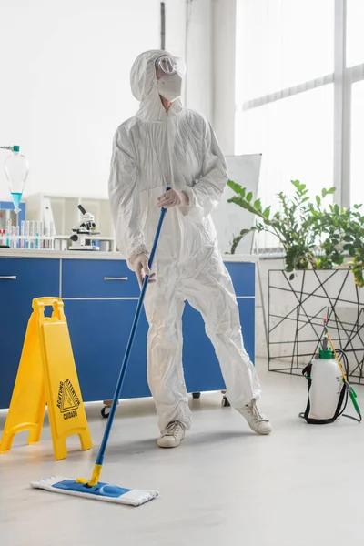 Scientist in hazmat suit looking away while cleaning floor in laboratory — Stock Photo