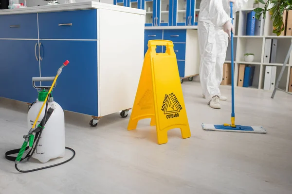 Abgeschnittene Ansicht eines Wissenschaftlers im Schutzanzug, der den Boden im Labor in der Nähe der Aufmerksamkeitstafel reinigt — Stockfoto