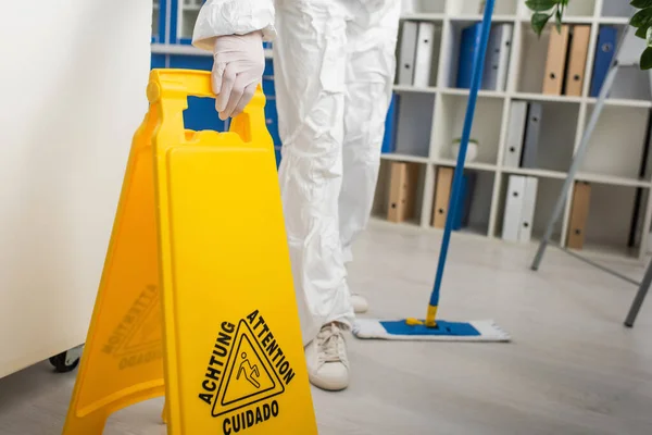 Ausgeschnittene Ansicht eines Arztes im Schutzanzug mit Aufmerksamkeitstafel und Wischmopp im Labor — Stockfoto