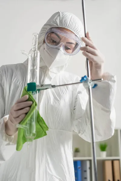 Femme en lunettes, masque médical et combinaison Hazmat essuyant trépied à la clinique — Photo de stock