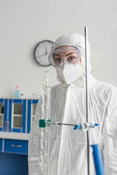 Médico en traje de materiales peligrosos y gafas mirando a la cámara en el laboratorio - foto de stock