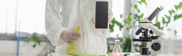 Частковий вид вченого, що тримає смартфон з порожнім екраном біля колби і мікроскопа, банер — стокове фото