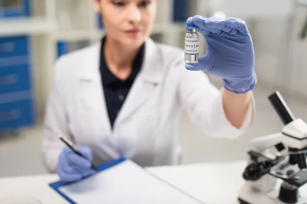 Médico borroso en guantes de látex que sostiene la vacuna contra el coronavirus en la clínica - foto de stock