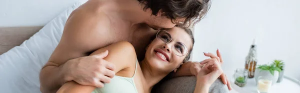 Shirtless man kissing smiling woman in top and eyeglasses on bed, banner — Stock Photo