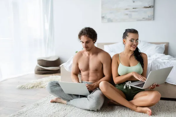 Sourire couple sexy en utilisant des ordinateurs portables près du lit à la maison — Photo de stock