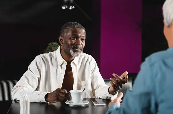 Homme afro-américain senior gestuelle lors d'une conversation avec un ami flou dans un pub — Photo de stock